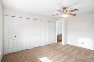 Unfurnished bedroom featuring multiple closets, light carpet, ensuite bath, and a ceiling fan