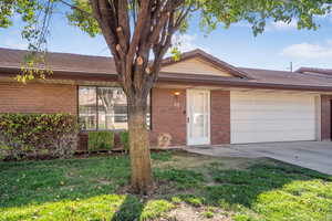 View of front of home featuring a front yard, driveway, an attached garage, and brick siding
