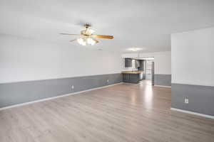 Unfurnished living room featuring light wood-style floors, a wainscoted wall, and ceiling fan