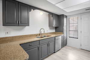 Kitchen featuring gray cabinetry, light stone counters, light wood-type flooring, and stainless steel dishwasher