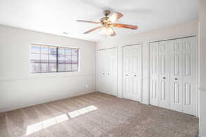 Unfurnished bedroom with multiple closets, carpet flooring, and a ceiling fan