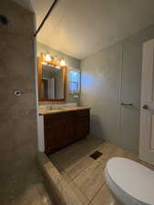 Bathroom with a textured ceiling, vanity, tiled shower, and a textured wall