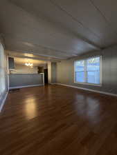 Unfurnished living room featuring a chandelier, dark wood-style flooring, and beamed ceiling