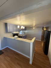 Kitchen featuring light countertops, a peninsula, freestanding refrigerator, pendant lighting, and dark wood-style floors