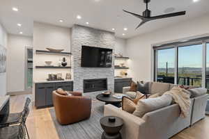 Living room featuring light wood-style flooring, a stone fireplace, recessed lighting, and a ceiling fan