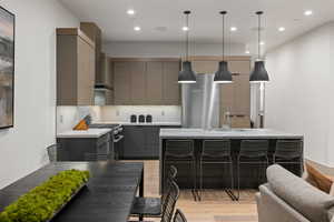 Kitchen featuring a breakfast bar area, appliances with stainless steel finishes, hanging light fixtures, light wood-type flooring, and an island with sink