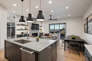 Kitchen featuring dark stone countertops, an island with sink, decorative light fixtures, light wood finished floors, and modern cabinets
