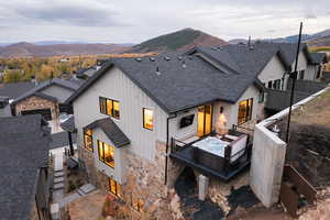 Rear view of property featuring roof with shingles, board and batten siding, stone siding, and a deck with mountain view