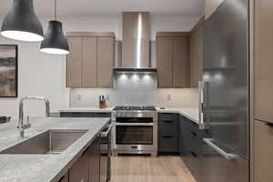 Kitchen featuring stainless steel appliances, wall chimney exhaust hood, pendant lighting, tasteful backsplash, and light stone counters