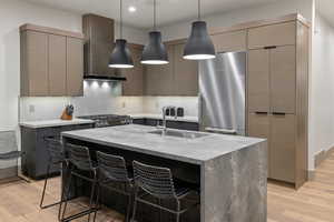 Kitchen with a kitchen bar, appliances with stainless steel finishes, light stone counters, decorative light fixtures, and a center island with sink