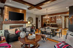 Living room featuring light wood finished floors, beamed ceiling, a fireplace, coffered ceiling, and a chandelier