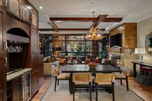 Dining space featuring a premium fireplace, light wood-type flooring, coffered ceiling, beam ceiling, and wine cooler