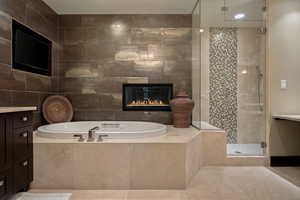 Full bathroom with vanity, a shower stall, a tiled fireplace, a garden tub, and tile patterned floors