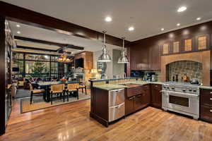 Kitchen with appliances with stainless steel finishes, light stone countertops, decorative light fixtures, dark brown cabinets, and light wood-style floors