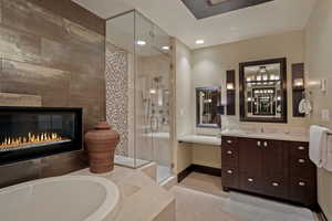 Full bath with vanity, light tile patterned floors, a stall shower, a garden tub, and a glass covered fireplace