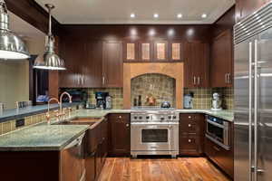 Kitchen with premium appliances, light stone counters, pendant lighting, light wood-style flooring, and recessed lighting