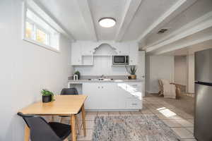 Kitchen featuring light countertops, appliances with stainless steel finishes, white cabinetry, light tile patterned flooring, and a textured ceiling