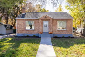 Bungalow featuring a front yard, roof with shingles, and brick siding