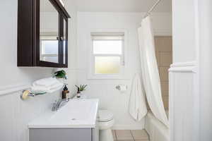 Full bath with a wainscoted wall, vanity, light tile patterned flooring, and shower / tub combo