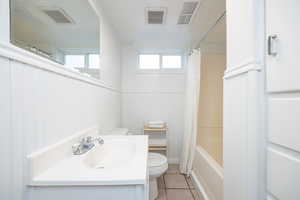Full bathroom featuring light tile patterned flooring, vanity, shower / tub combo, and wainscoting