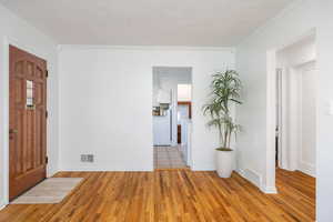 Entrance foyer with ornamental molding, light wood-style flooring, and a textured ceiling