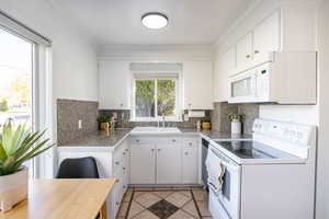 Kitchen featuring white appliances, white cabinets, light tile patterned floors, tile countertops, and ornamental molding