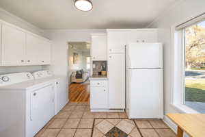 Laundry area with crown molding, washer and clothes dryer, and light tile patterned flooring