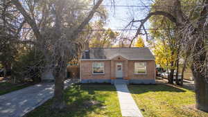 Bungalow featuring driveway, brick siding, a shingled roof, and a chimney