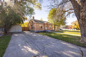 View of front of home with brick siding, a storage unit, a chimney, and driveway