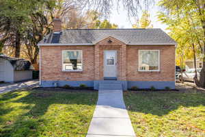 Bungalow-style home featuring a front yard, a shingled roof, and a chimney
