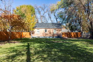 Rear view of house with a fenced backyard, a chimney, and brick siding