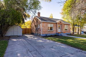 Bungalow with a storage unit, brick siding, a shingled roof, and a chimney