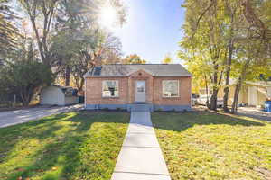 Bungalow-style house featuring brick siding, a chimney, a storage shed, and a front lawn