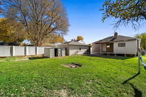 Back of house with a storage unit, a fenced backyard, a chimney, and roof with shingles