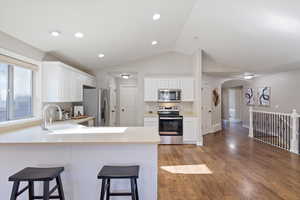 Kitchen featuring light countertops, dark wood finished floors, appliances with stainless steel finishes, arched walkways, and white cabinets