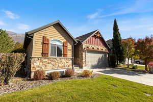 View of front of house featuring board and batten siding, driveway, stone siding, an attached garage, and a front lawn