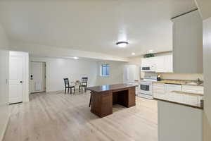 Kitchen featuring white cabinets, white appliances, light wood-type flooring, a breakfast bar, and dark stone counters