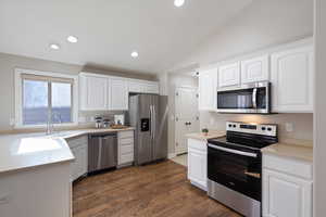 Kitchen featuring appliances with stainless steel finishes, lofted ceiling, white cabinets, light countertops, and dark wood-style flooring
