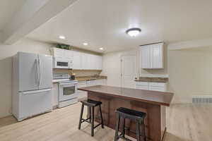 Kitchen featuring white appliances, light wood-style flooring, a breakfast bar area, white cabinets, and recessed lighting