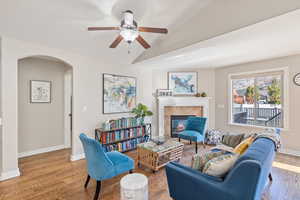 Living area with wood finished floors, a tile fireplace, arched walkways, a ceiling fan, and vaulted ceiling