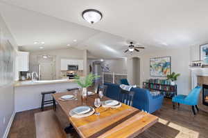 Dining area with vaulted ceiling, dark wood finished floors, a tile fireplace, arched walkways, and a ceiling fan