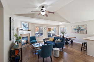 Living area featuring dark wood-style flooring, a fireplace, vaulted ceiling, and a ceiling fan