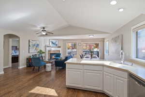 Kitchen with stainless steel dishwasher, dark wood-style floors, arched walkways, a fireplace, and a peninsula