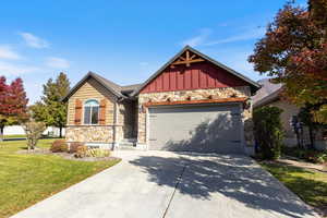 Craftsman-style home featuring stone siding, board and batten siding, driveway, a front lawn, and an attached garage