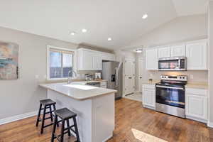 Kitchen with appliances with stainless steel finishes, light countertops, white cabinetry, a kitchen bar, and lofted ceiling