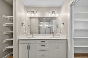 Full bathroom featuring wood finished floors, double vanity, a stall shower, a walk in closet, and a textured ceiling