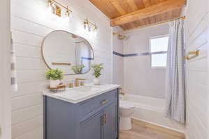 Bathroom featuring light wood-style floors, shower / bathtub combination with curtain, vanity, wooden walls, and a wooden ceiling with exposed beams