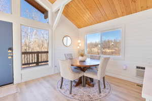 Dining room featuring light wood-style floors, wood walls, wooden ceiling, high vaulted ceiling, and a wall mounted AC