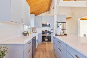 Kitchen featuring wood ceiling, light wood-type flooring, appliances with stainless steel finishes, and light stone counters