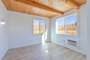 Bedroom with wood walls, light wood-type flooring, a wood ceiling with exposed beams, and an AC wall unit